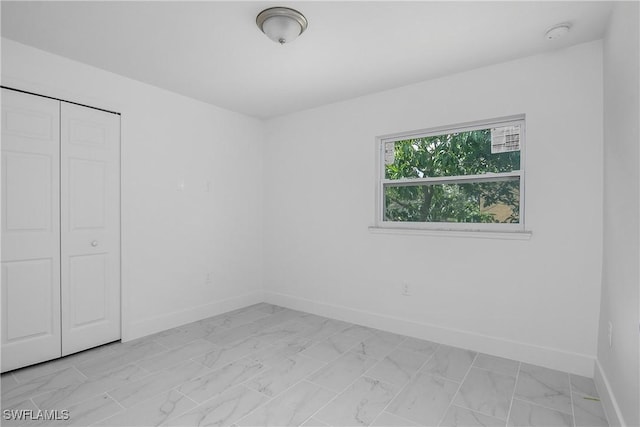 unfurnished bedroom with marble finish floor, baseboards, and a closet