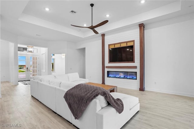 living room featuring a tray ceiling, light wood-type flooring, visible vents, and recessed lighting