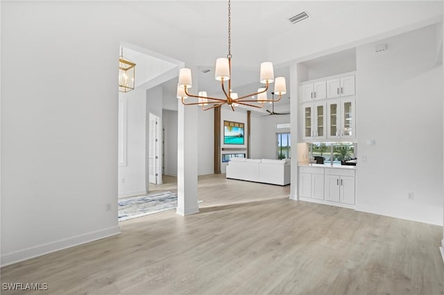 unfurnished dining area with an inviting chandelier, visible vents, light wood-style flooring, and baseboards
