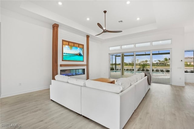 living area featuring a tray ceiling, light wood-style flooring, ceiling fan, and recessed lighting