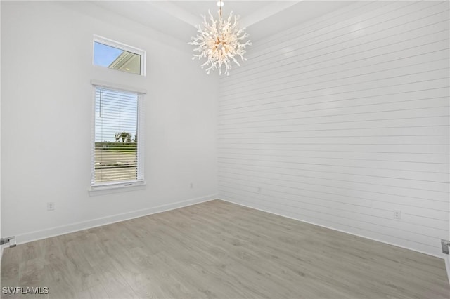 unfurnished room featuring baseboards, a raised ceiling, a notable chandelier, and wood finished floors