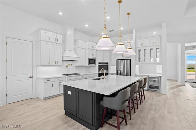 kitchen featuring wine cooler, light wood-style flooring, a sink, white cabinetry, and appliances with stainless steel finishes