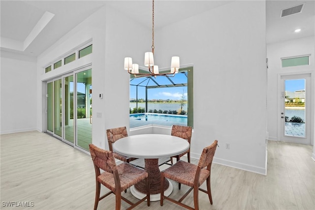 dining area featuring plenty of natural light, a water view, light wood-style flooring, and a high ceiling