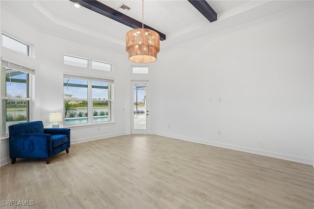 interior space featuring beam ceiling, light wood-type flooring, a chandelier, a high ceiling, and baseboards