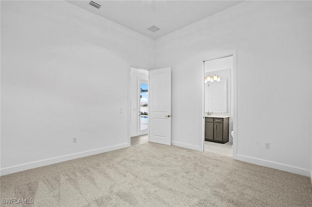 unfurnished bedroom featuring light colored carpet, ensuite bath, and baseboards