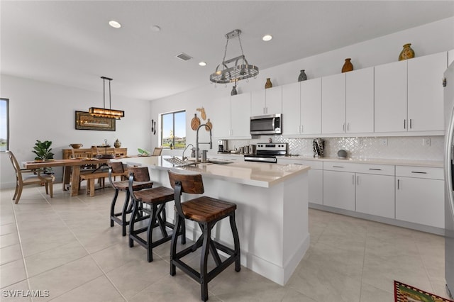 kitchen with a breakfast bar area, hanging light fixtures, stainless steel appliances, light countertops, and backsplash