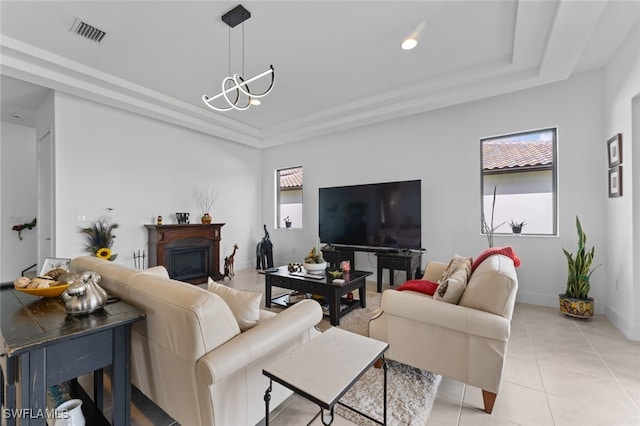 living area with light tile patterned floors, visible vents, baseboards, a tray ceiling, and a glass covered fireplace