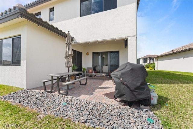 rear view of property featuring a patio area, a yard, and stucco siding