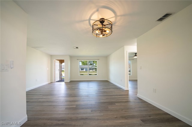 unfurnished living room with visible vents, baseboards, dark wood-style floors, and ceiling fan with notable chandelier