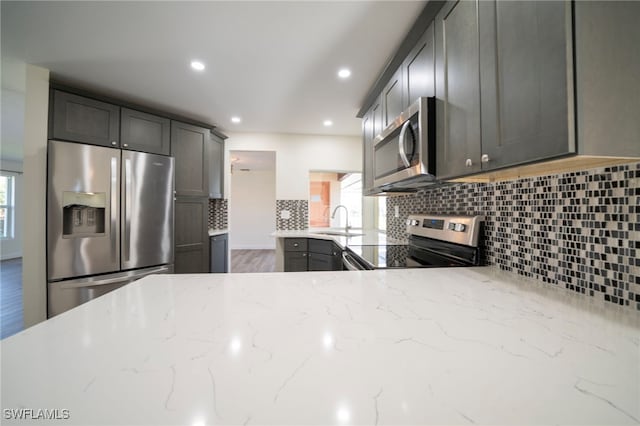 kitchen with light stone counters, a sink, tasteful backsplash, wood finished floors, and stainless steel appliances