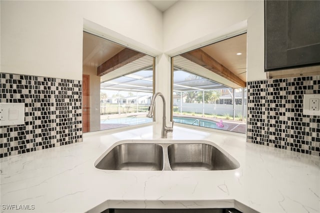 room details with backsplash, light stone countertops, and a sink