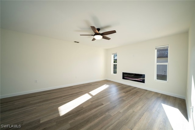 unfurnished living room featuring a glass covered fireplace, baseboards, ceiling fan, and wood finished floors