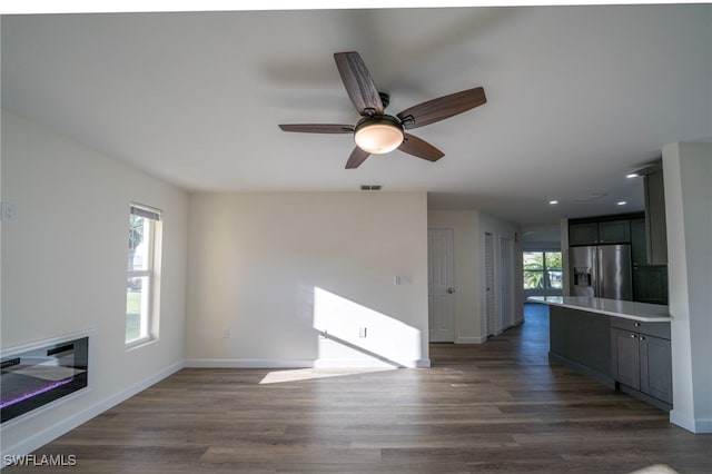 unfurnished living room with plenty of natural light, ceiling fan, and dark wood finished floors