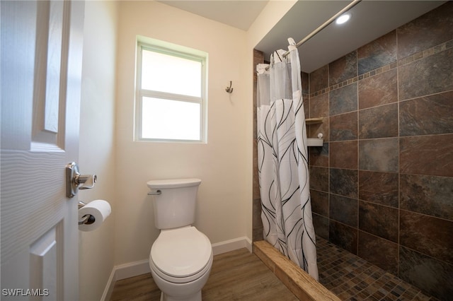 full bathroom with tiled shower, toilet, baseboards, and wood finished floors