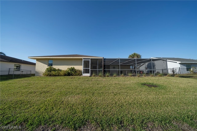 rear view of house with stucco siding, a lawn, a lanai, and fence