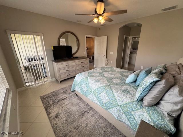 bedroom featuring light tile patterned floors, visible vents, arched walkways, baseboards, and ceiling fan