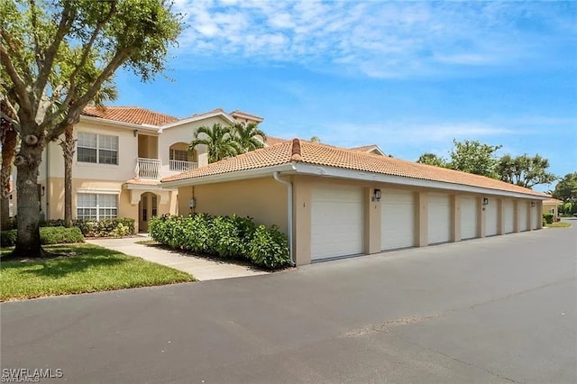 mediterranean / spanish-style home with a tiled roof, community garages, a balcony, and stucco siding