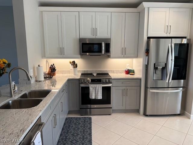 kitchen with appliances with stainless steel finishes, gray cabinets, a sink, and light stone countertops