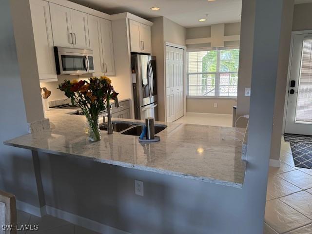 kitchen featuring light tile patterned floors, white cabinets, appliances with stainless steel finishes, a peninsula, and light stone countertops