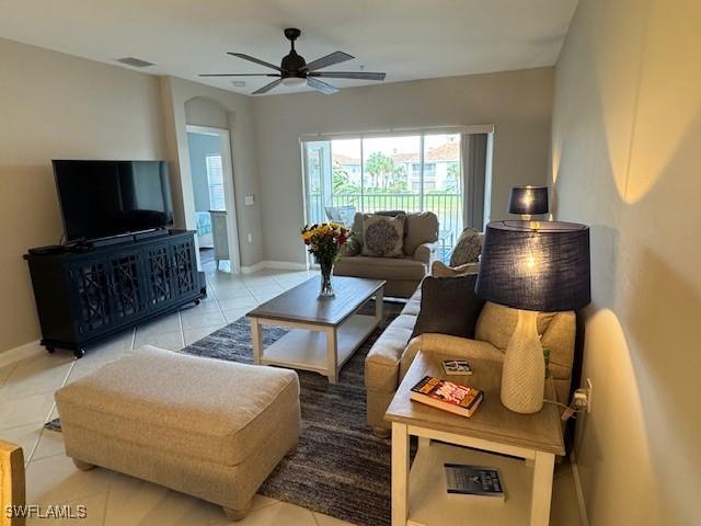 tiled living room featuring arched walkways, visible vents, ceiling fan, and baseboards