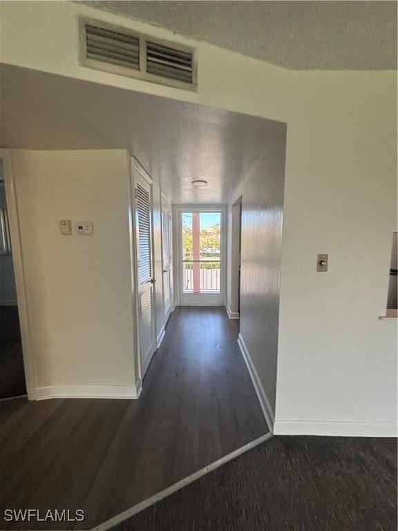 hallway featuring a textured ceiling, dark wood finished floors, visible vents, and baseboards