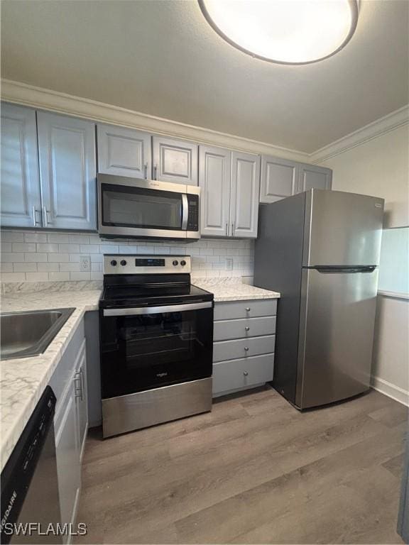 kitchen with crown molding, gray cabinets, light wood-style flooring, appliances with stainless steel finishes, and a sink