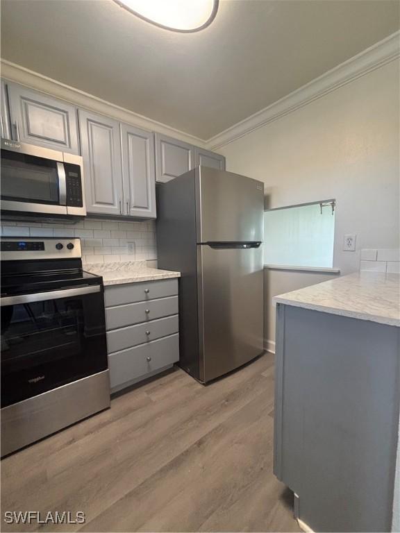 kitchen with ornamental molding, appliances with stainless steel finishes, backsplash, gray cabinets, and light wood finished floors