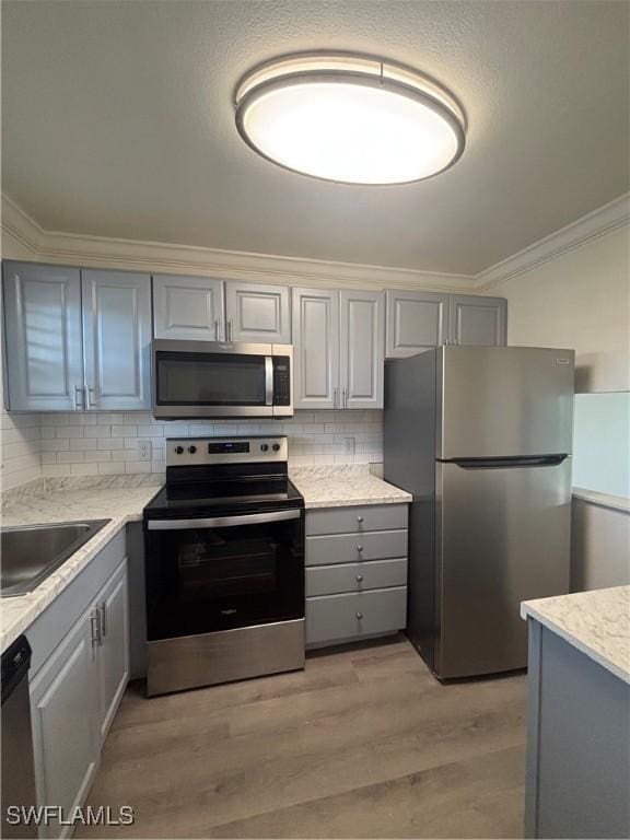 kitchen with a sink, stainless steel appliances, ornamental molding, and gray cabinets