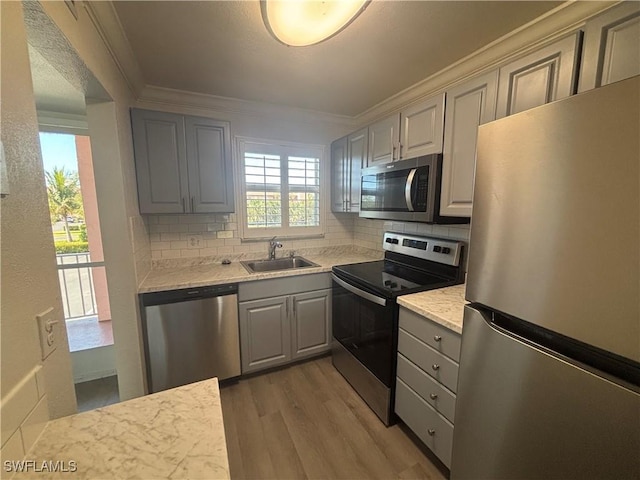 kitchen with ornamental molding, stainless steel appliances, gray cabinetry, light wood-style floors, and a sink