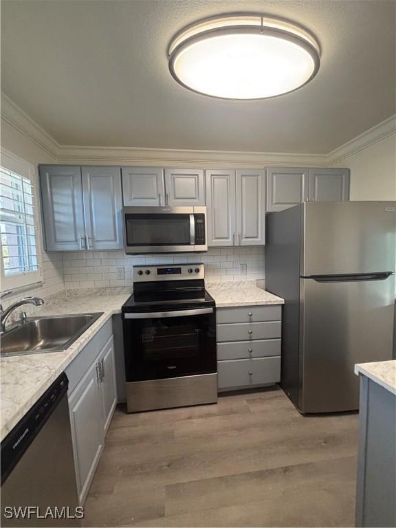 kitchen featuring stainless steel appliances, gray cabinets, a sink, and ornamental molding