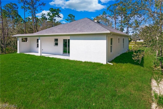 back of property with stucco siding, roof with shingles, a lawn, and a patio