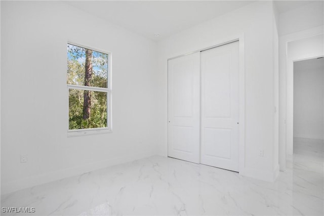 unfurnished bedroom with marble finish floor, a closet, and baseboards