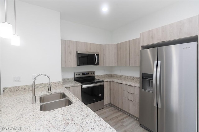 kitchen with light stone counters, stainless steel appliances, a sink, and light brown cabinetry