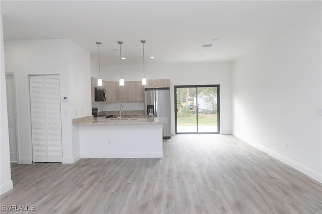 kitchen with appliances with stainless steel finishes, light wood-type flooring, open floor plan, and a peninsula