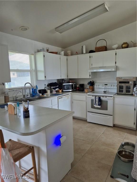 kitchen featuring light tile patterned floors, under cabinet range hood, white appliances, a sink, and white cabinets