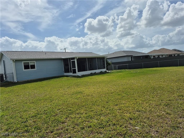 rear view of property with central air condition unit, a sunroom, fence, and a lawn