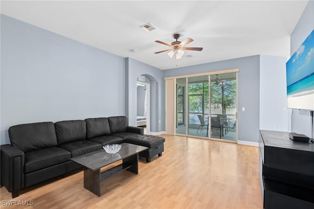 living room with a ceiling fan, visible vents, baseboards, light wood finished floors, and arched walkways