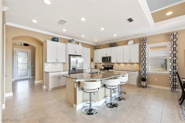 kitchen featuring visible vents, an island with sink, a sink, a kitchen breakfast bar, and stainless steel appliances