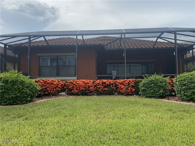 rear view of house featuring a tile roof, a yard, and a lanai