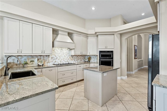 kitchen with decorative backsplash, arched walkways, custom exhaust hood, black appliances, and a sink