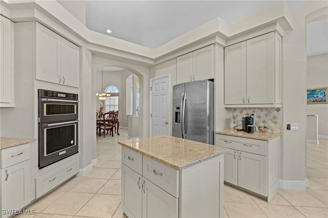 kitchen featuring double wall oven, backsplash, stainless steel fridge, arched walkways, and light tile patterned floors