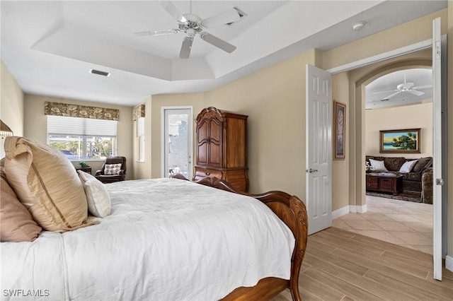 bedroom with visible vents, a tray ceiling, light wood-style floors, baseboards, and ceiling fan