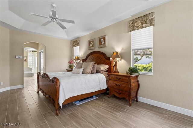 bedroom with arched walkways, multiple windows, baseboards, and wood tiled floor