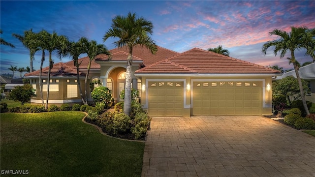 mediterranean / spanish house with decorative driveway, a tile roof, an attached garage, and stucco siding