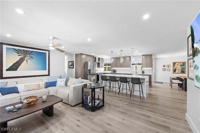 living room featuring a ceiling fan, light wood-type flooring, baseboards, and recessed lighting