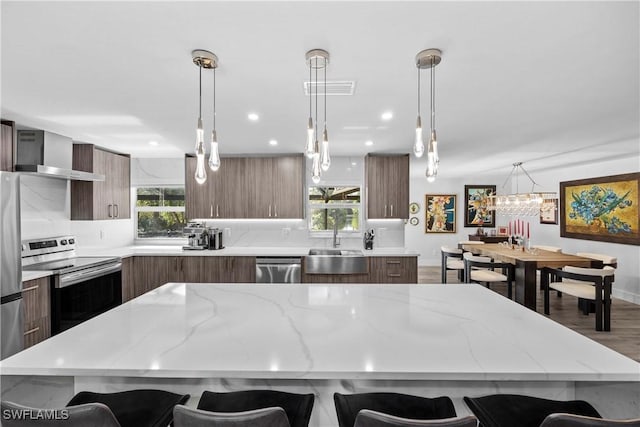 kitchen featuring stainless steel appliances, wall chimney range hood, a breakfast bar area, and modern cabinets