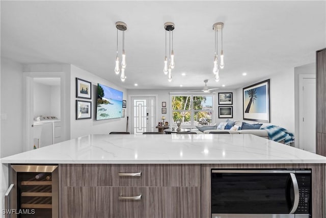 kitchen featuring beverage cooler, washer and clothes dryer, stainless steel microwave, light stone counters, and open floor plan