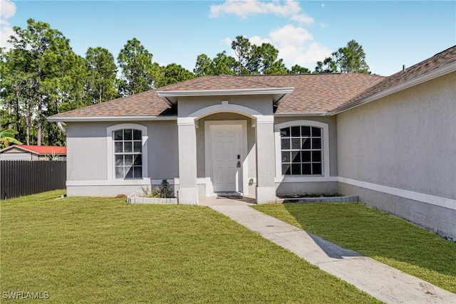 doorway to property featuring a shingled roof, a lawn, fence, and stucco siding