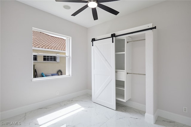 unfurnished bedroom with a barn door, baseboards, marble finish floor, and a ceiling fan