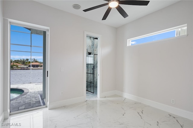 empty room with marble finish floor, a ceiling fan, and baseboards